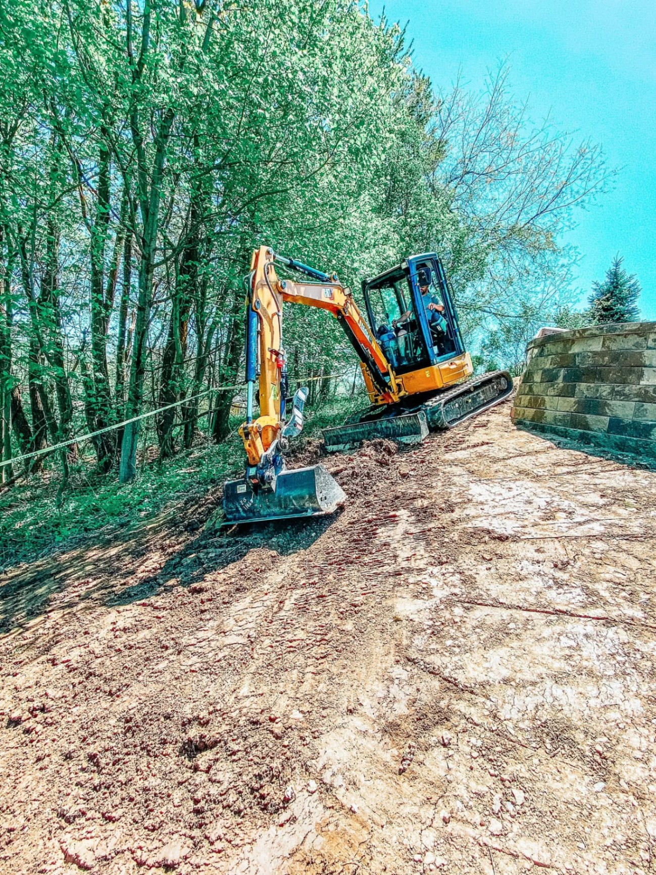 CAT 304E2 excavator moving a large boulder on a wooded property